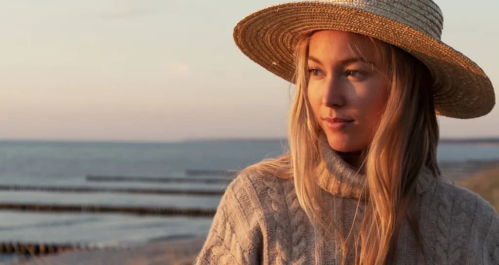 Žena sa slamnatim šeširom na morskoj obali u suton